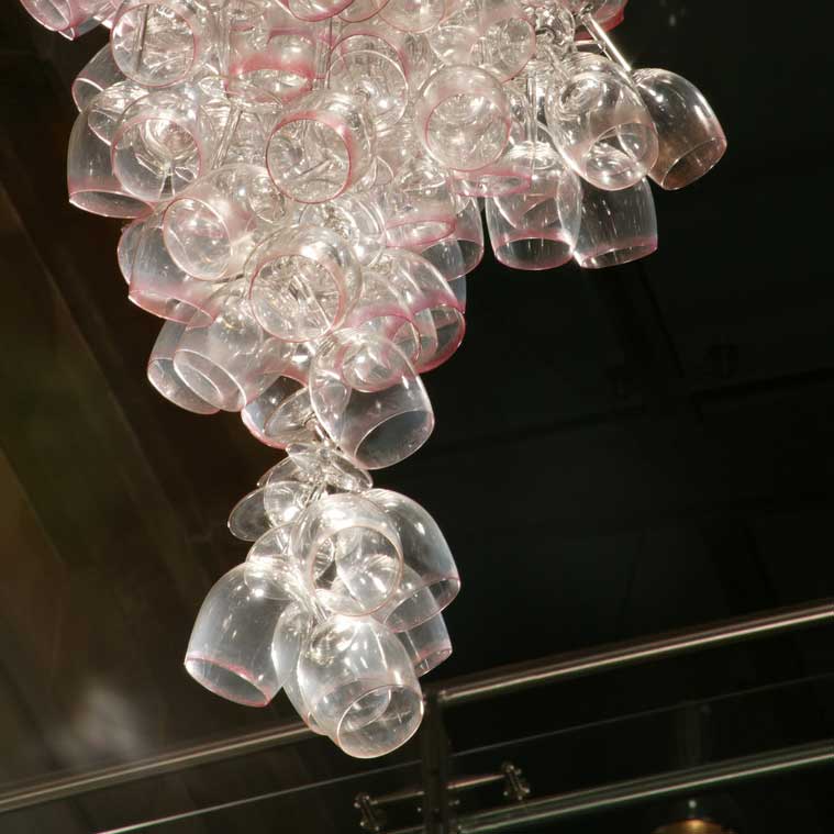 Here Come the Girls 2009
Manchester Art Gallery Atrium
1100 Wine Glasses
Lipstick
Commissioned by Manchester Art Gallery to celebrate the festive season and specifically to link to their exhibition Angels of Anarchy: Women Artists and Surrealism. The primary reference is to Meret Oppenheim's iconic fur teacup, saucer and spoon, Object. In a contemporary culture where women are just as likely to drink wine as tea the vessel still functions as a metaphor for the female body, but in the 21st century sexual politics have evolved.
Each glass is individually rimmed with lipstick using the artist's lips. Cosmetics, particularly lipstick, are often advertised as a way to enhance feminine power and choice, and one cosmetic company even used the slogan 'It's not makeup, it's ammunition'.
<em>"While thinking of 'strong women' femininity, power and Christmastime, I was reminded of the recent Boots TV commercials with crowds of women getting glammed up and marching out to celebrate to the Sugababes 'Here come the Girls'."</em> Susie MacMurray
The work offers a space for rumination on the evolution of feminism and perceptions of female power/empowerment in it's various guises – cultural/political/sexual. Also on the different ways women choose to exercise that empowerment (including binge drinking), the ambiguities it throws up, and psychological bargains we strike with ourselves.